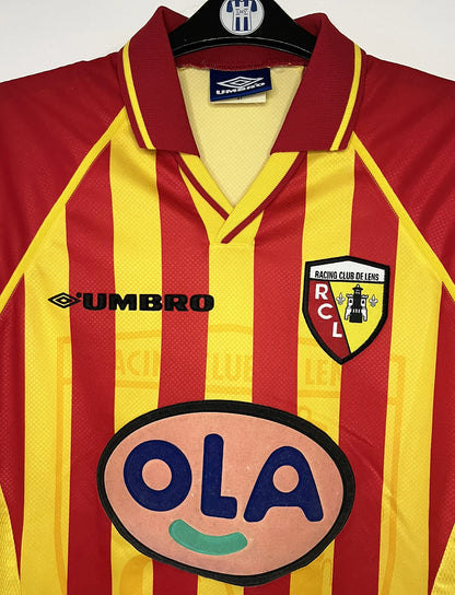 Maillot de foot vintage domicile jaune et rouge du RC Lens de la saison 1998/1999. On peut retrouver l'équipementier Umbro et le sponsor OLA. Il s'agit d'un maillot authentique d'époque.