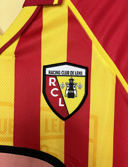 Maillot de foot vintage domicile jaune et rouge du RC Lens de la saison 1998/1999. On peut retrouver l'équipementier Umbro et le sponsor OLA. Il s'agit d'un maillot authentique d'époque.