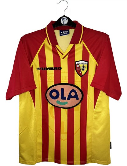 Maillot de foot vintage domicile jaune et rouge du RC Lens de la saison 1998/1999. On peut retrouver l'équipementier Umbro et le sponsor OLA. Il s'agit d'un maillot authentique d'époque.