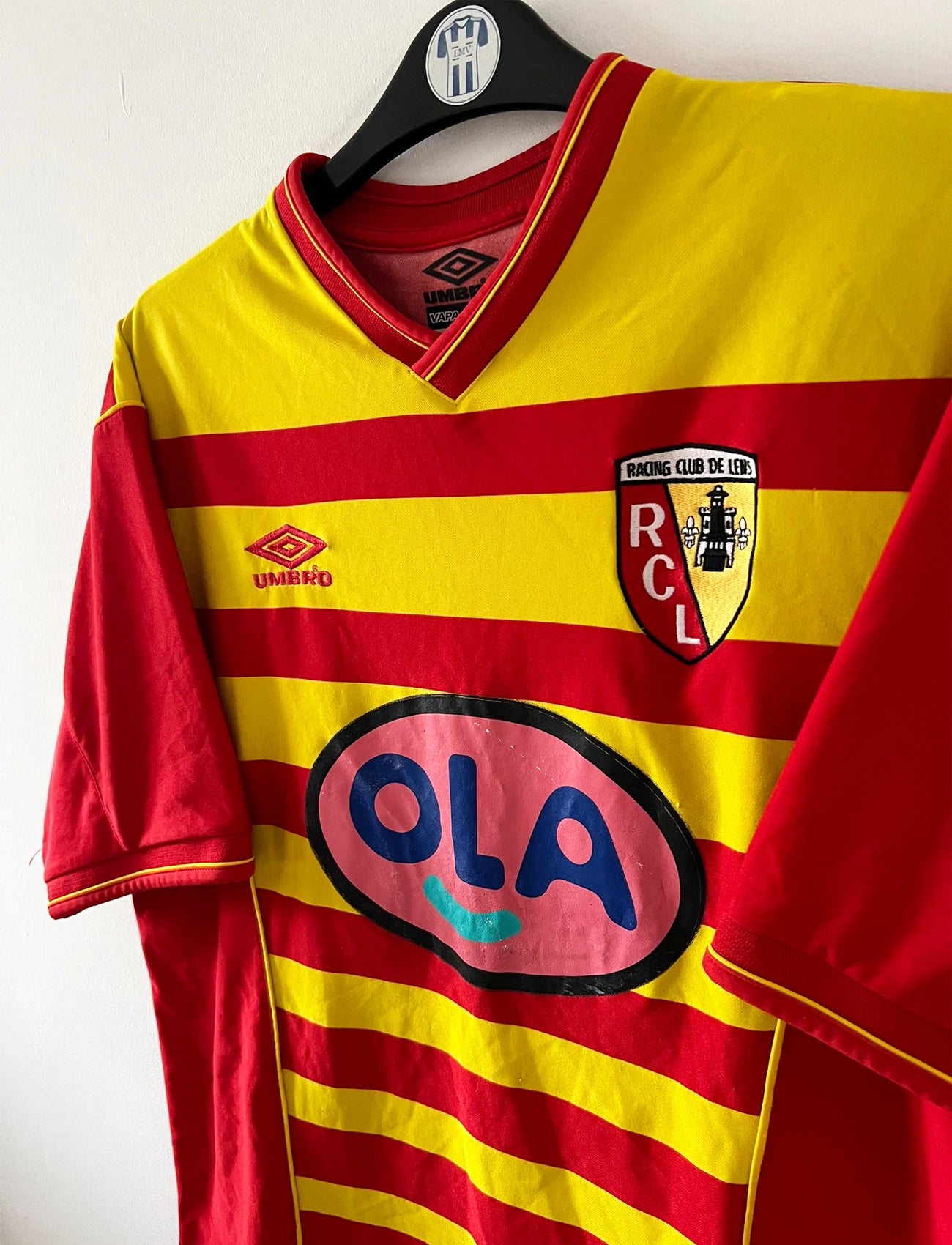 Maillot foot vintage rouge et jaune du RC Lens de la saison 2000/2001. On peut retrouver l'équipementier Umbro et le sponsor OLA. Il s'agit d'un maillot authentique d'époque.