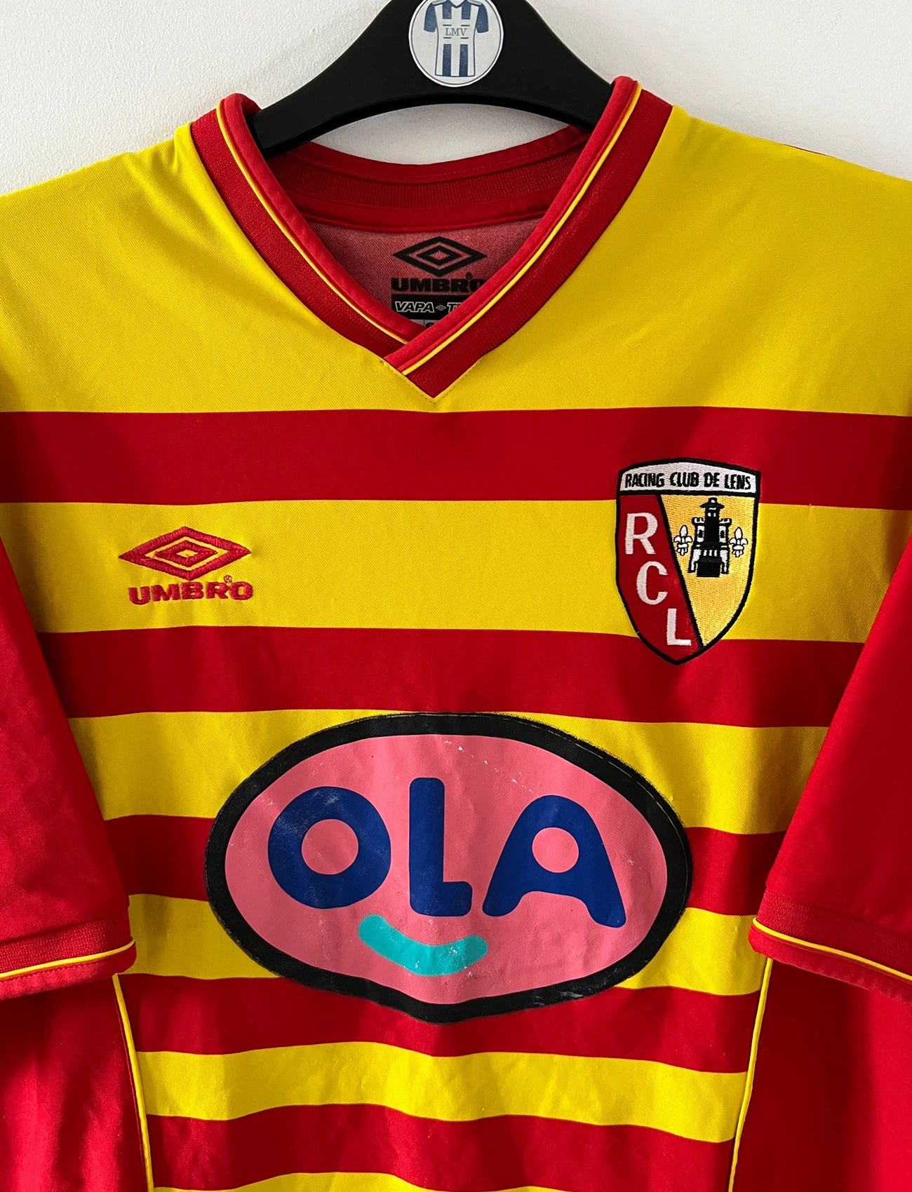 Maillot foot vintage rouge et jaune du RC Lens de la saison 2000/2001. On peut retrouver l'équipementier Umbro et le sponsor OLA. Il s'agit d'un maillot authentique d'époque.