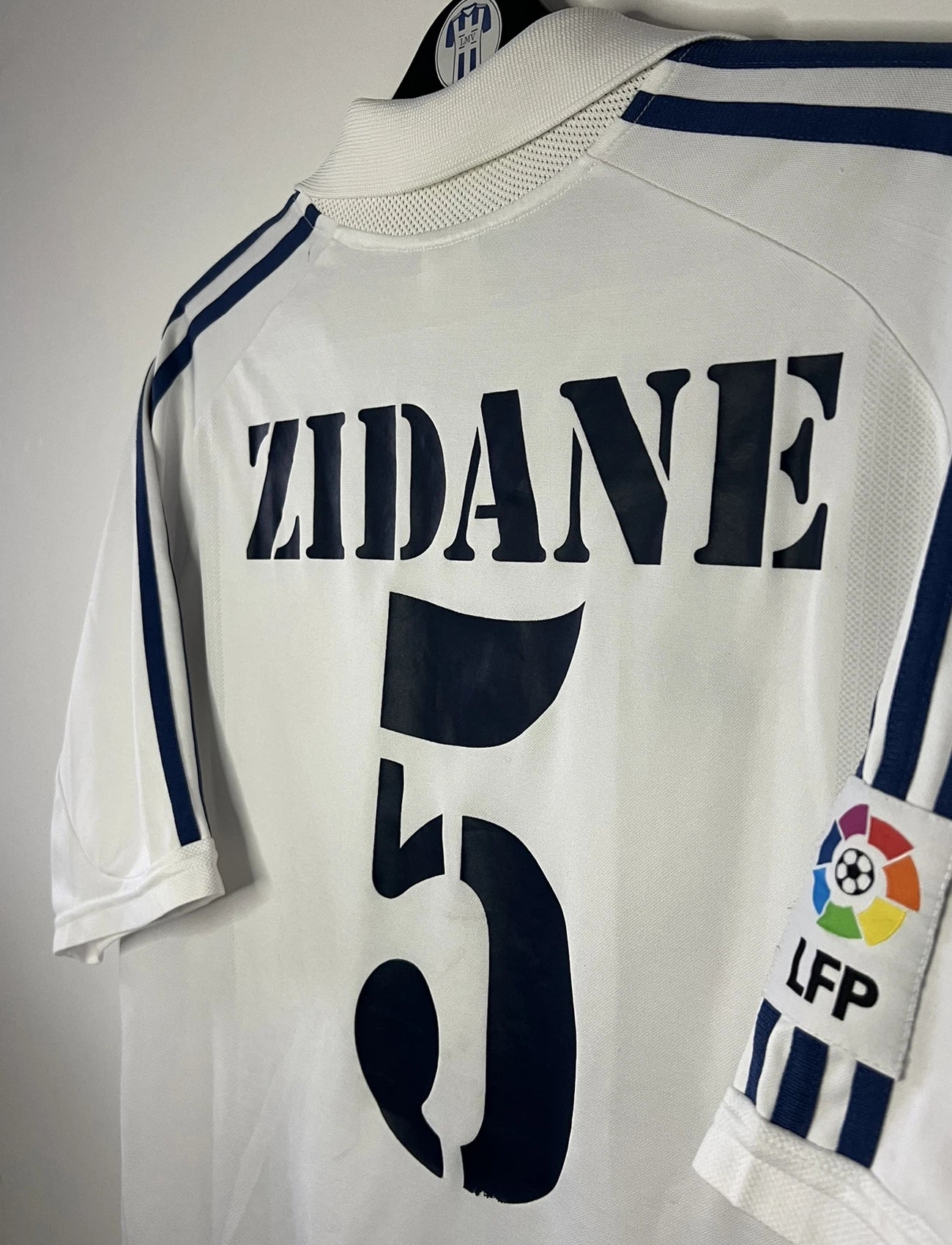 Maillot de foot vintage domicile du real madrid de la saison 2001-2002. Le maillot est de couleur blanc et noir. On peut retrouver l'équipementier adidas et le sponsor Real Madrid.com. Le maillot est floqué du numéro 5 Zinedine Zidane. Il s'agit d'un maillot authentique comportant les numéros 695856