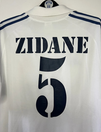 Maillot de foot vintage domicile du real madrid de la saison 2001-2002. Le maillot est de couleur blanc et noir. On peut retrouver l'équipementier adidas et le sponsor Real Madrid.com. Le maillot est floqué du numéro 5 Zinedine Zidane. Il s'agit d'un maillot authentique comportant les numéros 695856
