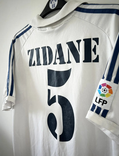 Maillot de foot vintage domicile du real madrid de la saison 2001-2002. Le maillot est de couleur blanc et noir. On peut retrouver l'équipementier adidas et le sponsor Real Madrid.com. Le maillot est floqué du numéro 5 Zinedine Zidane. Il s'agit d'un maillot authentique comportant les numéros 695856