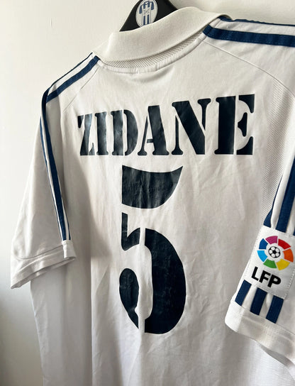 Maillot de foot vintage domicile blanc du real madrid de la saison 2001/2002. On peut retrouver l'équipementier Adidas et le sponsor Real madrid.com. Le maillot est floqué du numéro 5 Zinedine Zidane. Il s'agit d'un maillot authentique d'époque.
