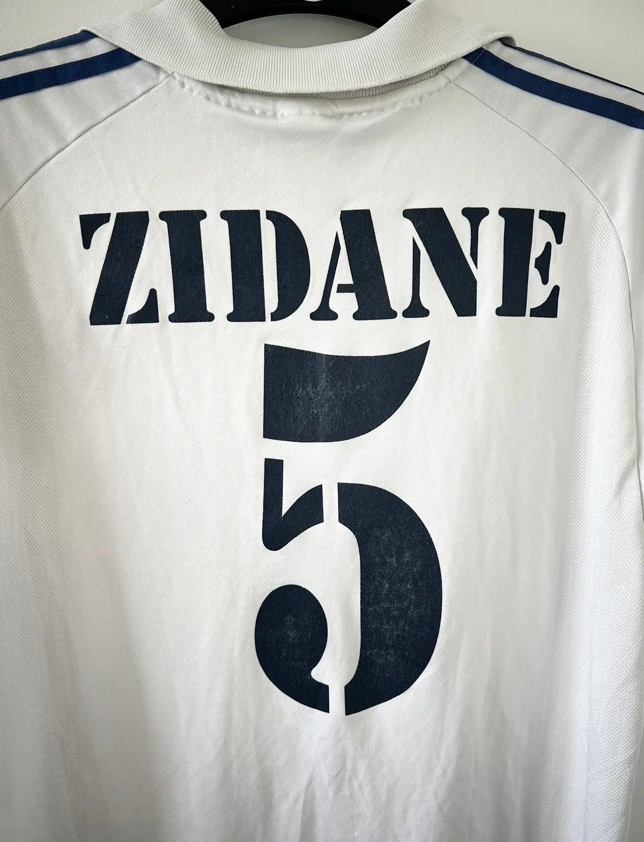 Maillot de foot vintage domicile du real madrid de la saison 2001-2002. Le maillot est de couleur blanc et noir. On peut retrouver l'équipementier adidas et le sponsor Real Madrid.com. Le maillot est floqué du numéro 5 Zinedine Zidane. Il s'agit d'un maillot authentique comportant les numéros 695856