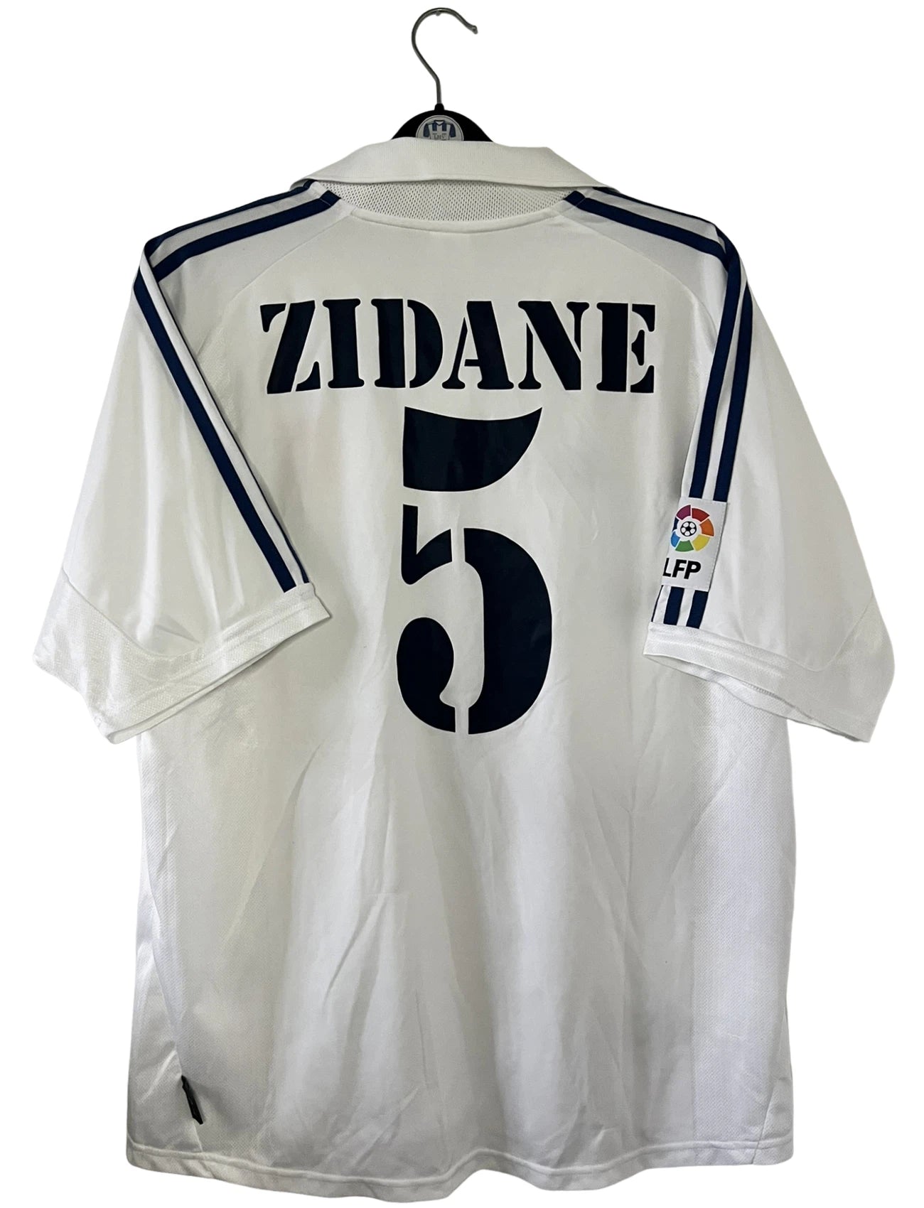 Maillot de foot vintage domicile blanc du real madrid de la saison 2001/2002. On peut retrouver l'équipementier Adidas et le sponsor Real madrid.com. Le maillot est floqué du numéro 5 Zinedine Zidane. Il s'agit d'un maillot authentique d'époque.
