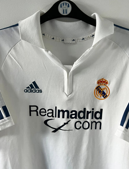 Maillot de foot vintage domicile blanc du real madrid de la saison 2001/2002. On peut retrouver l'équipementier Adidas et le sponsor Real Madrid.com. Le maillot est floqué du numéro 5 Zinedine Zidane. Il s'agit d'un maillot authentique d'époque.