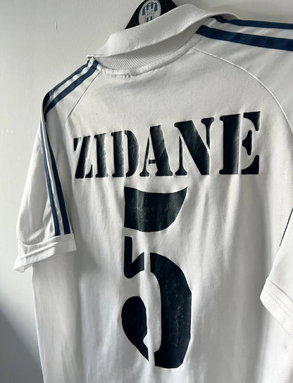 Maillot de foot vintage domicile blanc du real madrid de la saison 2001/2002. On peut retrouver l'équipementier Adidas et le sponsor Real Madrid.com. Le maillot est floqué du numéro 5 Zinedine Zidane. Il s'agit d'un maillot authentique d'époque.