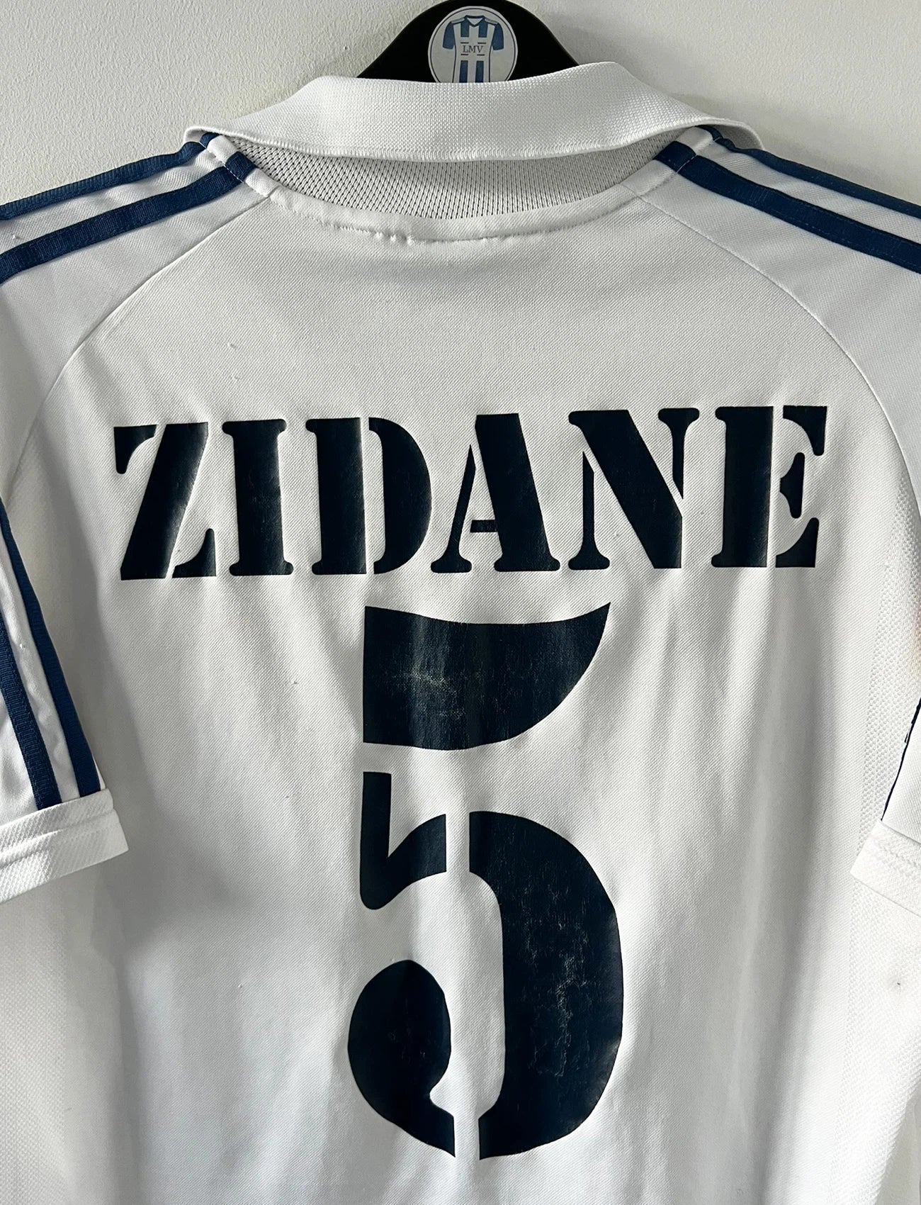 Maillot de foot vintage domicile blanc du real madrid de la saison 2001/2002. On peut retrouver l'équipementier Adidas et le sponsor Real Madrid.com. Le maillot est floqué du numéro 5 Zinedine Zidane. Il s'agit d'un maillot authentique d'époque.