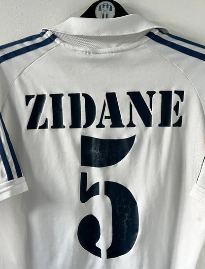 Maillot de foot vintage domicile blanc du real madrid de la saison 2001/2002. On peut retrouver l'équipementier Adidas et le sponsor Real Madrid.com. Le maillot est floqué du numéro 5 Zinedine Zidane. Il s'agit d'un maillot authentique d'époque.