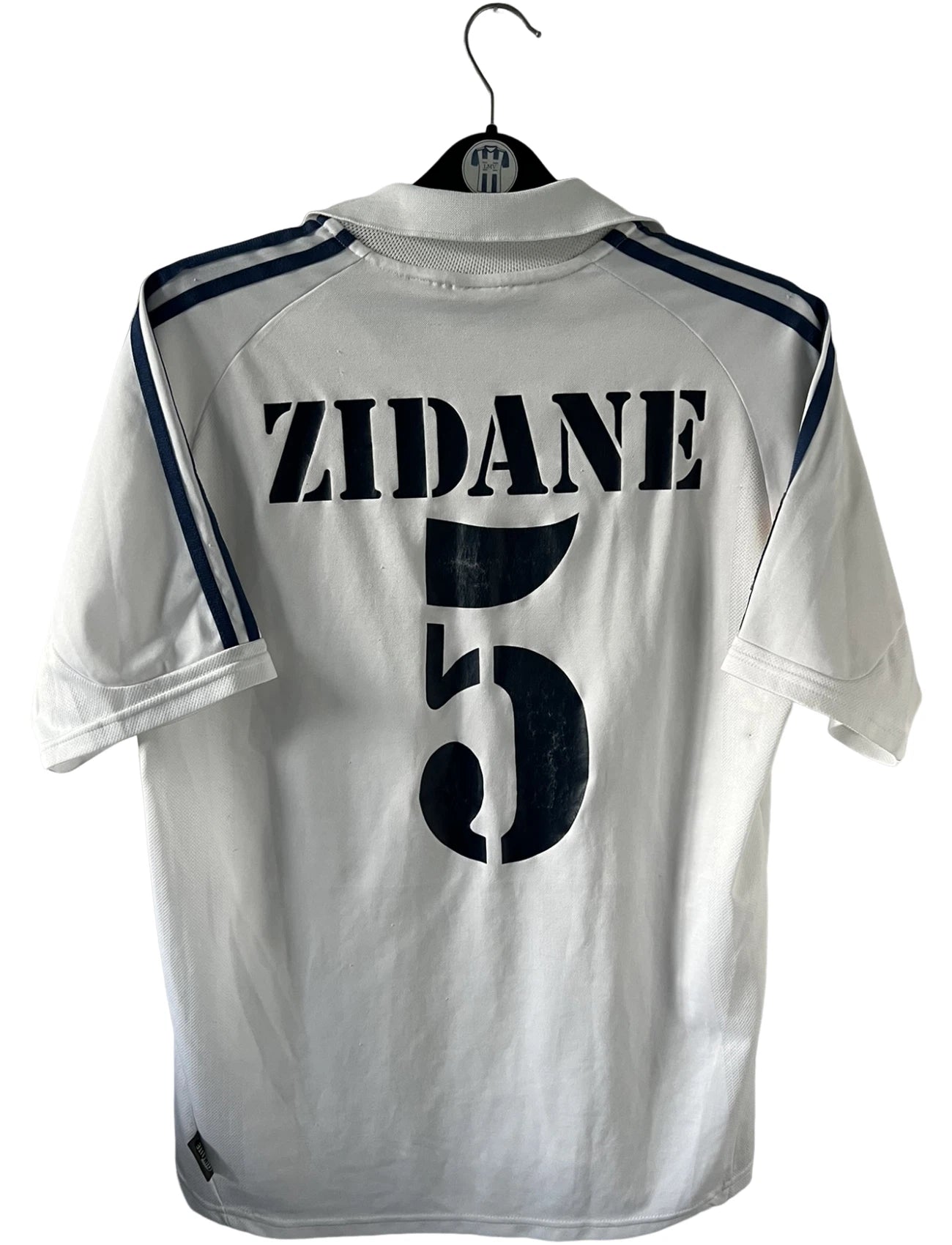 Maillot de foot vintage domicile blanc du real madrid de la saison 2001/2002. On peut retrouver l'équipementier Adidas et le sponsor Real Madrid.com. Le maillot est floqué du numéro 5 Zinedine Zidane. Il s'agit d'un maillot authentique d'époque.