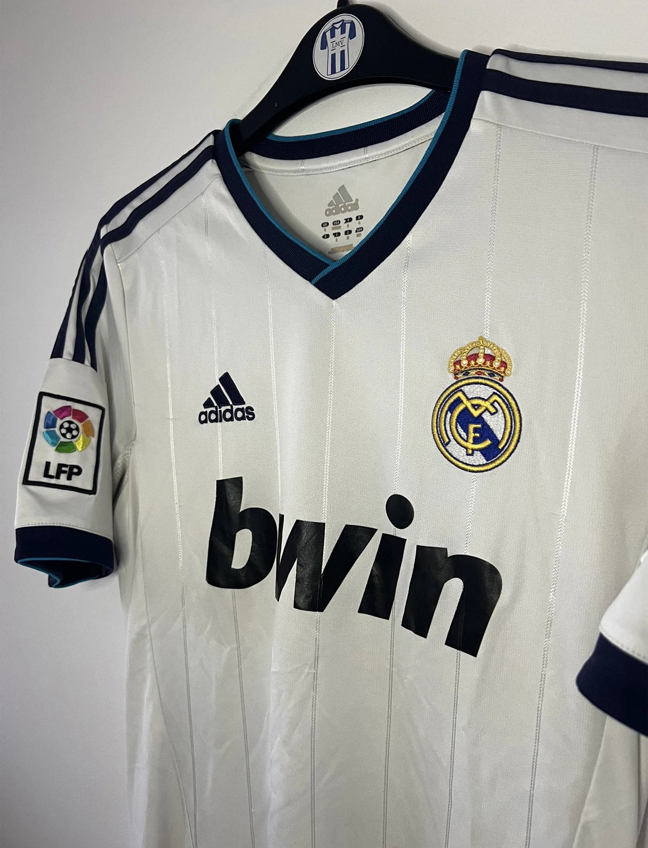 Maillot de foot vintage domicile blanc du real madrid de la saison 2012/2013. On peut retrouver l'équipementier adidas et le sponsor bwin. Le maillot est floqué du numéro 7 Cristiano Ronaldo. Il s'agit d'un maillot authentique comportant les numéros X21987.