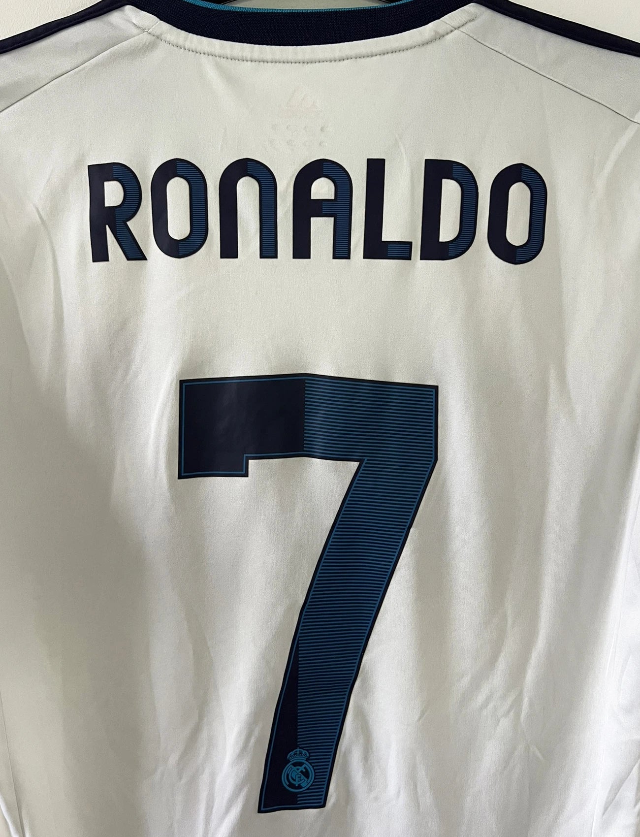 Maillot de foot vintage domicile blanc du real madrid de la saison 2012/2013. On peut retrouver l'équipementier adidas et le sponsor bwin. Le maillot est floqué du numéro 7 Cristiano Ronaldo. Il s'agit d'un maillot authentique comportant les numéros X21987.