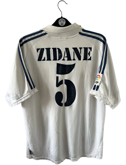 Maillot de foot vintage domicile blanc du Real Madrid de la saison 2001/2002. On peut retrouver l'équipementier Adidas et le sponsor Real Madrid.com. Le maillot est floqué du numéro 5 Zinedine Zidane. Il s'agit d'un maillot authentique d'époque.