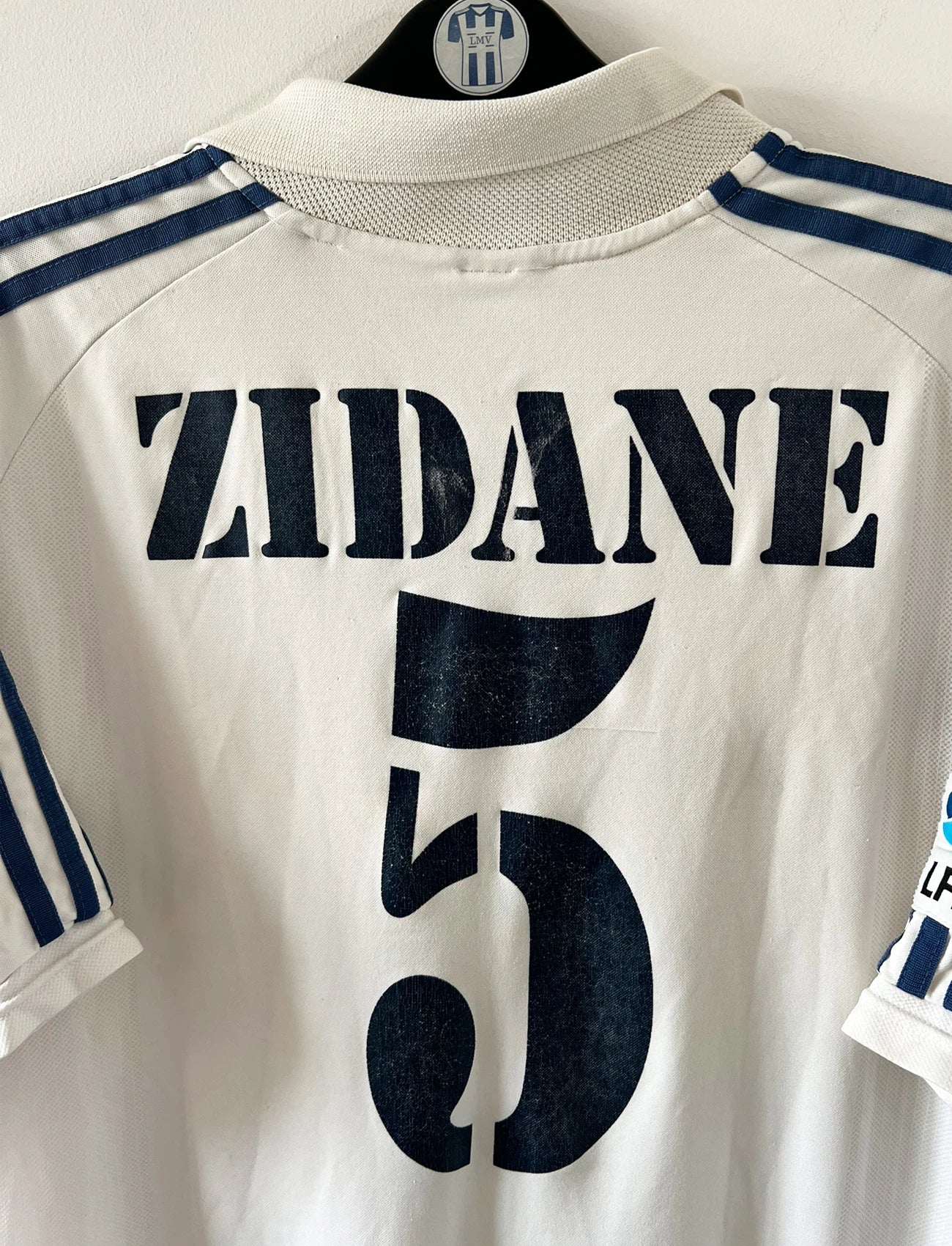 Maillot de foot vintage domicile blanc du Real Madrid de la saison 2001/2002. On peut retrouver l'équipementier Adidas et le sponsor Real Madrid.com. Le maillot est floqué du numéro 5 Zinedine Zidane. Il s'agit d'un maillot authentique d'époque.