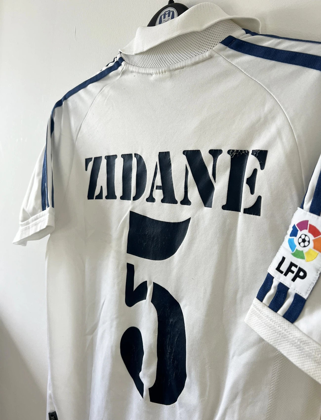 Maillot de foot vintage domicile blanc du real madrid de la saison 2001/2002. On peut retrouver l'équipementier Adidas et le sponsor Rea Madrid. Le maillot est floqué du numéro 5 Zinedine Zidane. Il s'agit d'un maillot authentique d'époque.