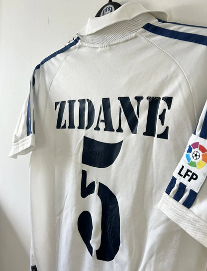 Maillot de foot vintage domicile blanc du real madrid de la saison 2001/2002. On peut retrouver l'équipementier Adidas et le sponsor Rea Madrid. Le maillot est floqué du numéro 5 Zinedine Zidane. Il s'agit d'un maillot authentique d'époque.