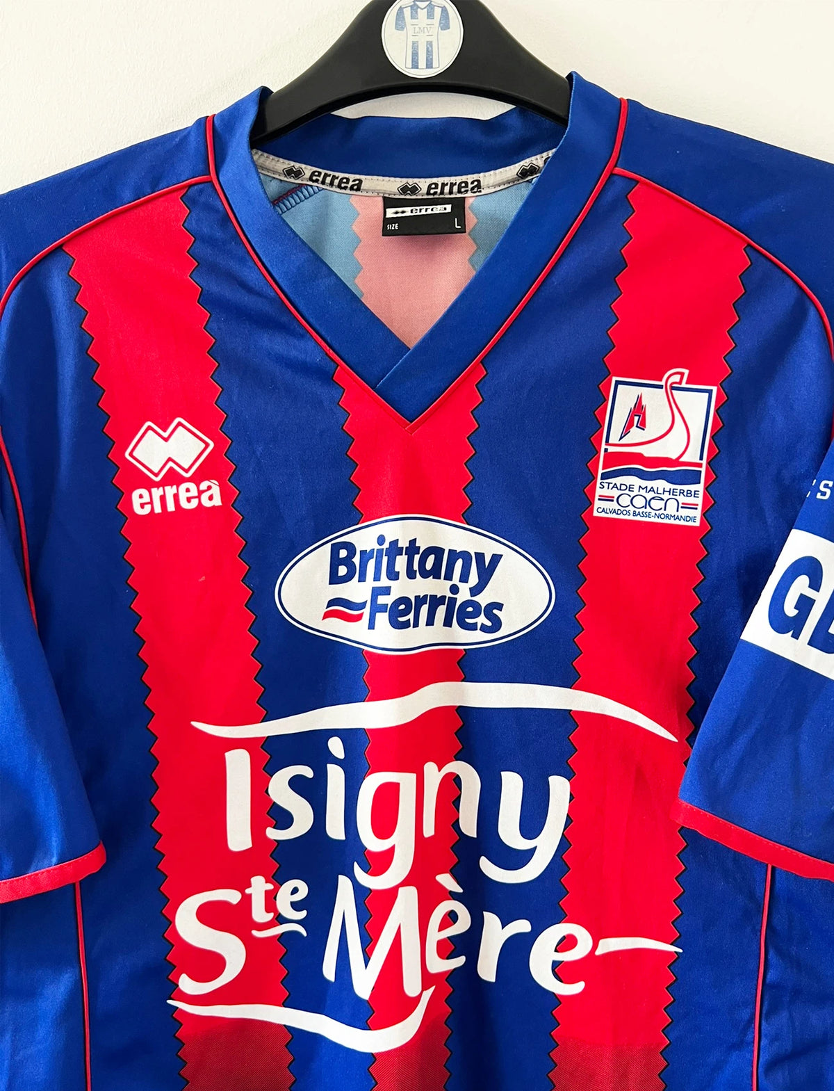 Maillot de foot vintage rouge et bleu du SM Caen de la saison 2004/2005. Il s'agit du maillot édité pour la finale de la Coupe de la Ligue. On peut retrouver les sponsors Isigny Ste Mère et Brittany Ferries. Il s'agit d'un maillot authentique d'époque.