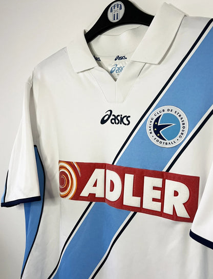 Maillot de foot vintage extérieur blanc du Racing Club de Strasbourg de la saison 2001/2003. On peut retrouver l'équipementier Asics et le sponsor Adler. Il s'agit d'un maillot authentique d'époque.
