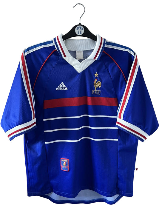 Maillot de foot vintage domicile bleu de l'équipe de france 1998. On peut retrouver l'équipementier Adidas. Le maillot est floqué du numéro 10 Zinedine Zidane. Il s'agit d'un maillot authentique d'époque.