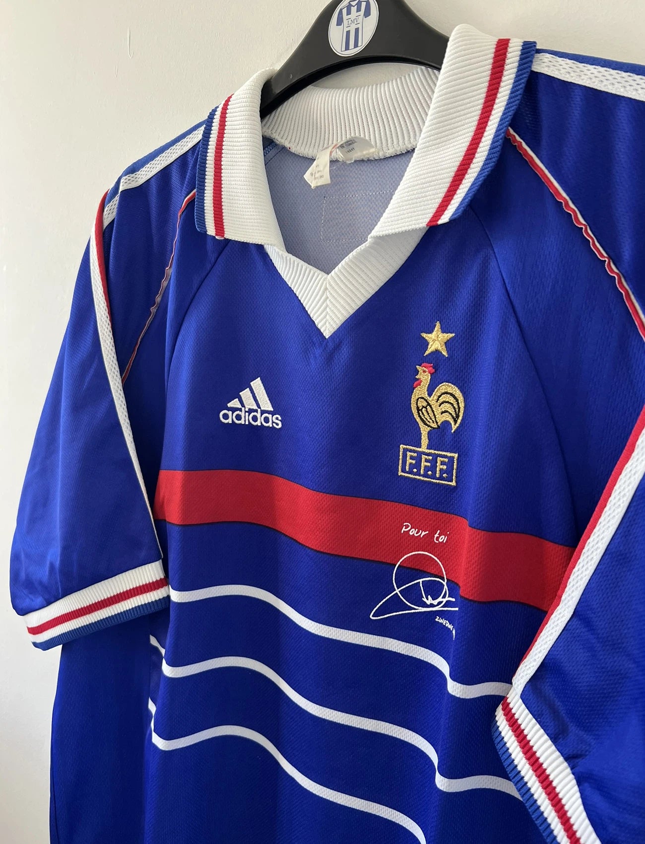 Maillot de foot vintage bleu blanc et rouge domicile de l'équipe de France 1998. On peut retrouver le sponsor adidas. On peut voir le coq sans l'étoile avec la signature "pour toi" de Zinedine Zidane. Il s'agit d'un maillot authentique.