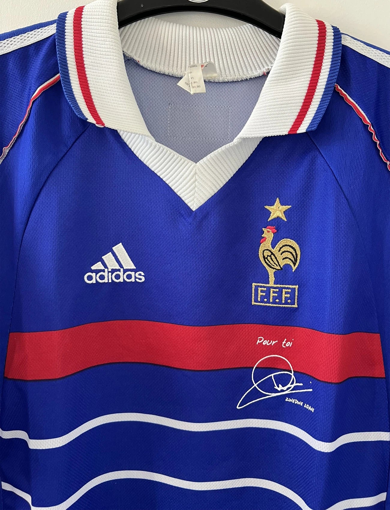 Maillot de foot vintage bleu blanc et rouge domicile de l'équipe de France 1998. On peut retrouver le sponsor adidas. On peut voir le coq sans l'étoile avec la signature "pour toi" de Zinedine Zidane. Il s'agit d'un maillot authentique.