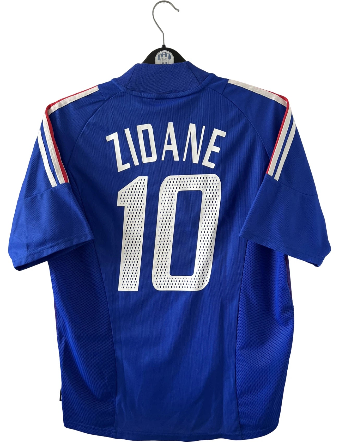 Maillot de foot vintage domicile bleu de l'équipe de france 2002. On peut retrouver l'équipementier Adidas. Le maillot est floqué du numéro 10 Zidane. Il s'agit d'un maillot authentique d'époque.