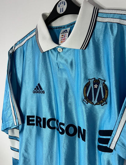 Maillot de foot vintage extérieur bleu de l'OM saison 1998/1999. On peut retrouver l'équipementier Adidas et le sponsor Ericsson. Il s'agit d'un maillot authentique d'époque.