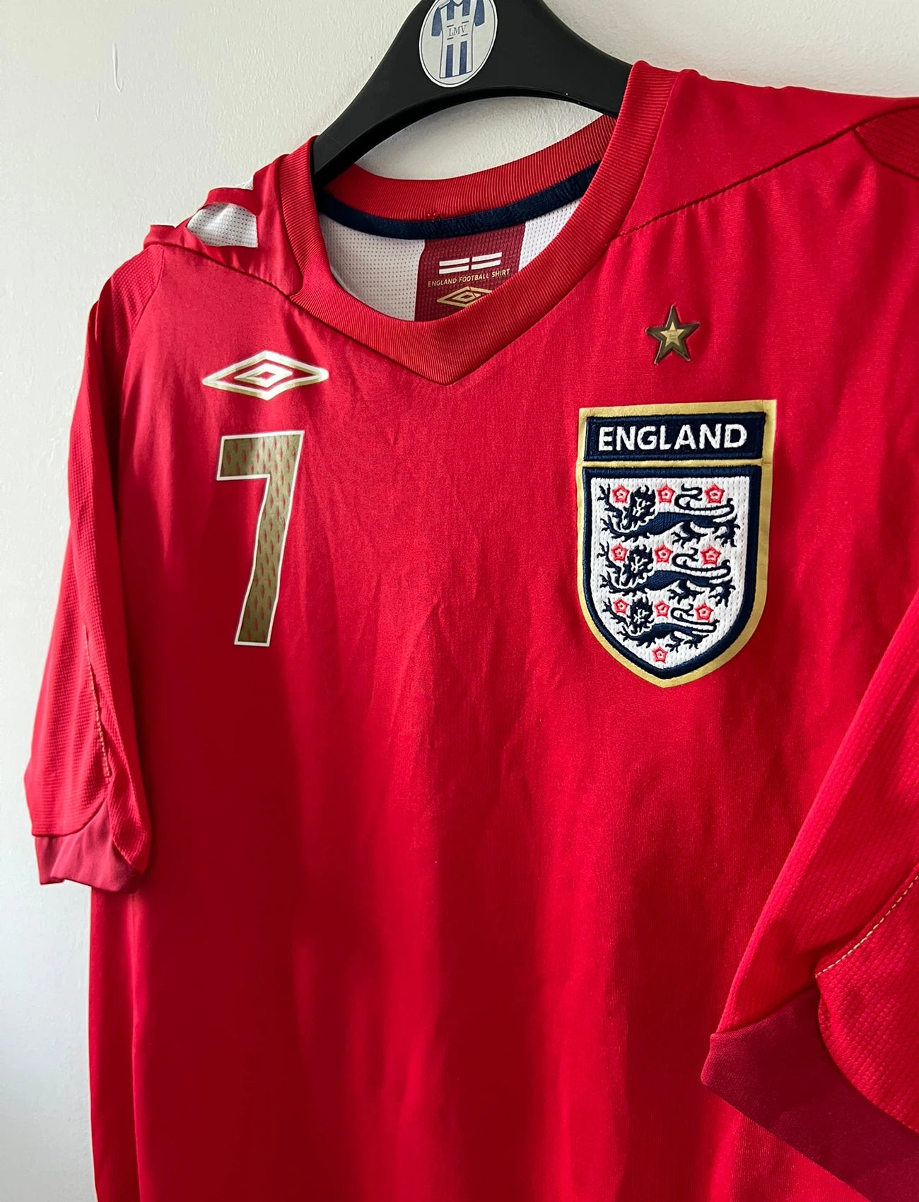 Maillot de foot vintage extérieur rouge de l'angleterre 2006/2008. On peut retrouver l'équipementier Umbro. Le maillot est floqué du numéro 7 David Beckham. Il s'agit d'un maillot authentique d'époque.