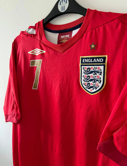 Maillot de foot vintage extérieur rouge de l'angleterre 2006/2008. On peut retrouver l'équipementier Umbro. Le maillot est floqué du numéro 7 David Beckham. Il s'agit d'un maillot authentique d'époque.