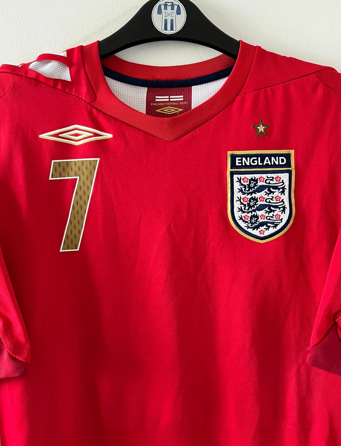 Maillot de foot vintage extérieur rouge de l'angleterre 2006/2008. On peut retrouver l'équipementier Umbro. Le maillot est floqué du numéro 7 David Beckham. Il s'agit d'un maillot authentique d'époque.