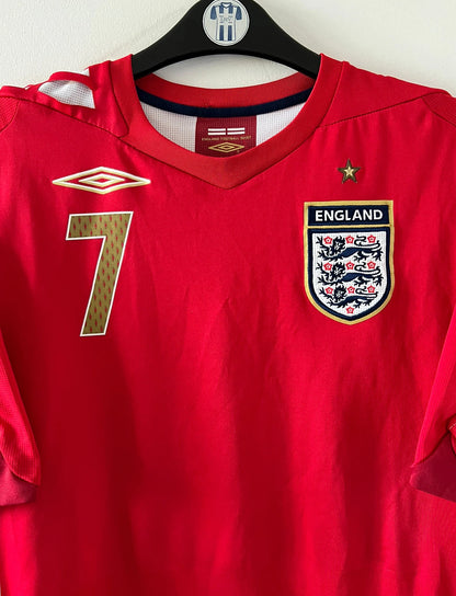 Maillot de foot vintage extérieur rouge de l'angleterre 2006/2008. On peut retrouver l'équipementier Umbro. Le maillot est floqué du numéro 7 David Beckham. Il s'agit d'un maillot authentique d'époque.