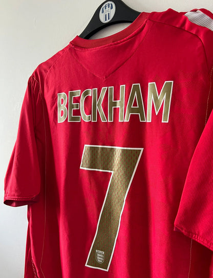Maillot de foot vintage extérieur rouge de l'angleterre 2006/2008. On peut retrouver l'équipementier Umbro. Le maillot est floqué du numéro 7 David Beckham. Il s'agit d'un maillot authentique d'époque.