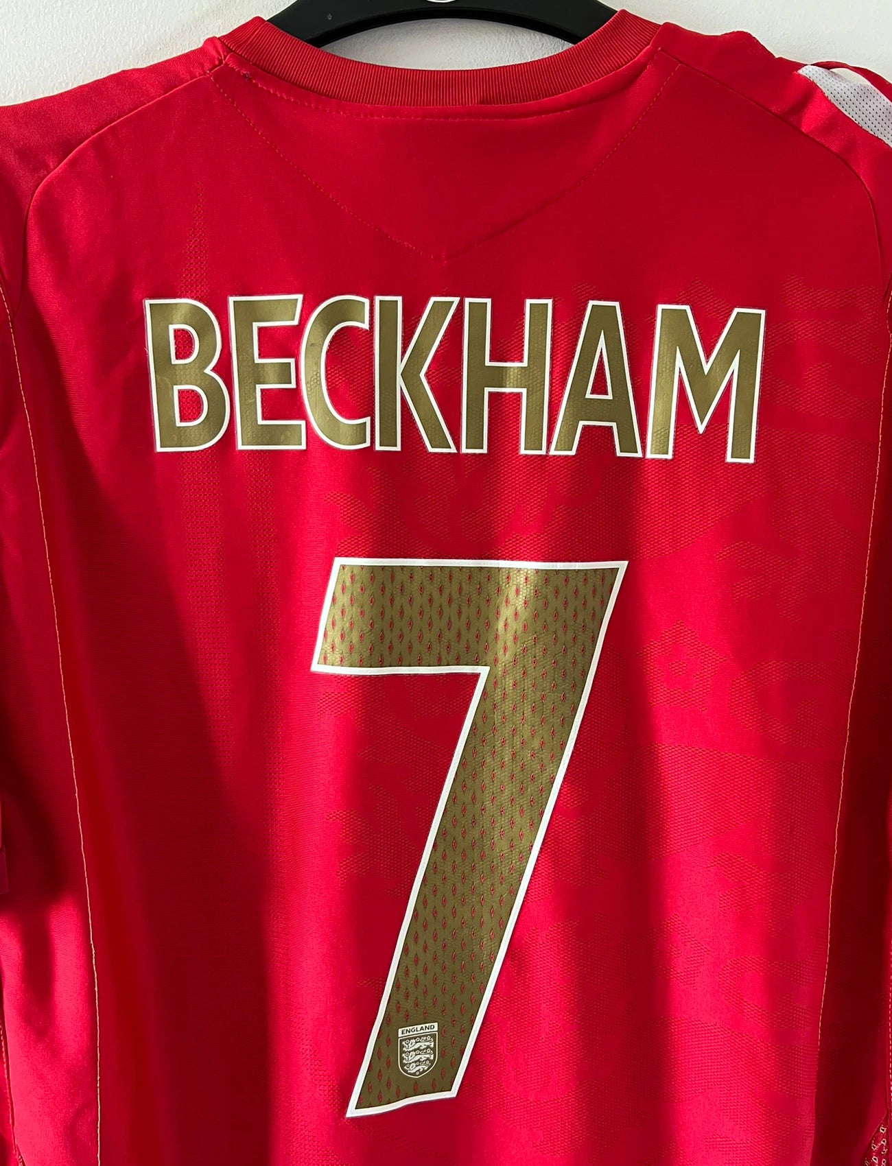 Maillot de foot vintage extérieur rouge de l'angleterre 2006/2008. On peut retrouver l'équipementier Umbro. Le maillot est floqué du numéro 7 David Beckham. Il s'agit d'un maillot authentique d'époque.