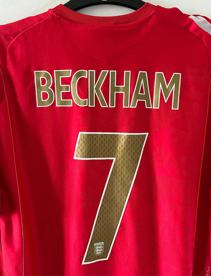 Maillot de foot vintage extérieur rouge de l'angleterre 2006/2008. On peut retrouver l'équipementier Umbro. Le maillot est floqué du numéro 7 David Beckham. Il s'agit d'un maillot authentique d'époque.