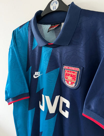 Maillot de foot vintage extérieur bleu d'arsenal de la saison 1995/1996. On peut retrouver l'équipementier Nike et le sponsor JVC. Il s'agit d'un maillot authentique d'époque.