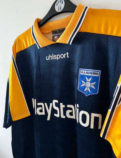 Maillot de foot vintage extérieur jaune et bleu de l'AJ Auxerre 2000/2001. On peut retrouver l'équipementier Uhlsport et le sponsor Playstation. Il s'agit d'un maillot authentique d'époque.