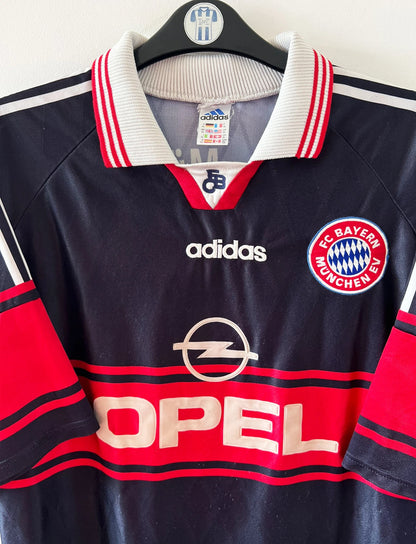 Maillot de foot vintage extérieur noir du Bayern Munich 1997/1998. On peut retrouver l'équipementier Adidas et le sponsor Opel. Le maillot est accompagné de son short d'époque. Il s'agit d'un maillot et d'un short authentique.