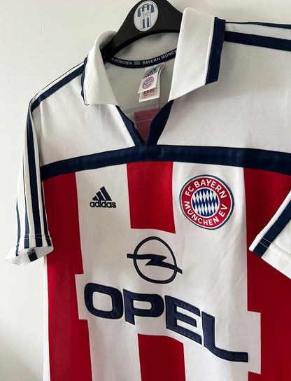 Maillot de foot vintage extérieur blanc du Bayern Munich de la saison 2000/2002. On peut retrouver l'équipementier Adidas et le sponsor Opel. Il s'agit d'un maillot authentique d'époque.