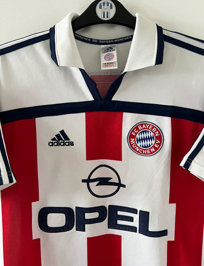 Maillot de foot vintage extérieur blanc du Bayern Munich de la saison 2000/2002. On peut retrouver l'équipementier Adidas et le sponsor Opel. Il s'agit d'un maillot authentique d'époque.