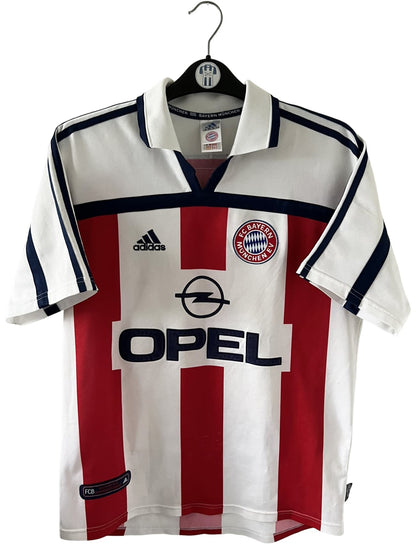 Maillot de foot vintage extérieur blanc du Bayern Munich de la saison 2000/2002. On peut retrouver l'équipementier Adidas et le sponsor Opel. Il s'agit d'un maillot authentique d'époque.