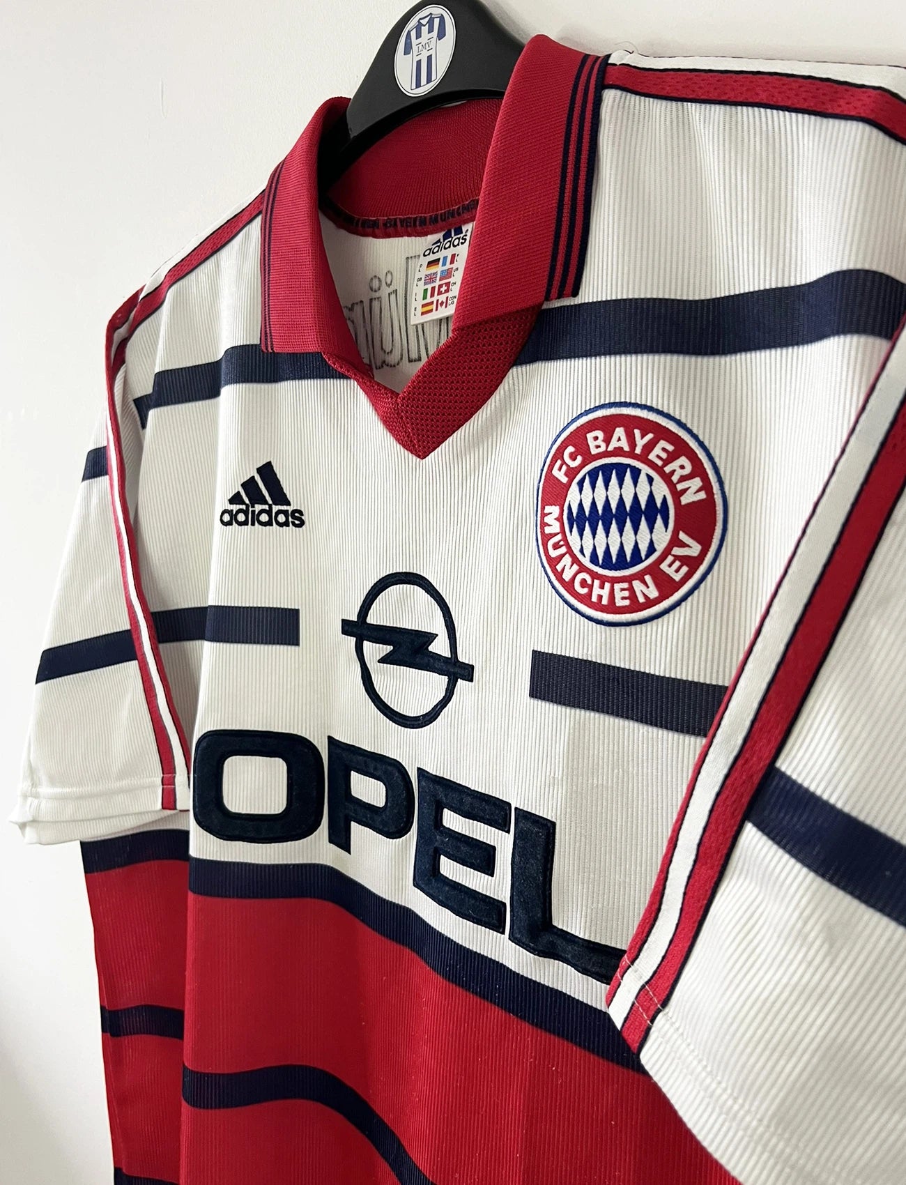 Maillot de foot vintage extérieur blanc et rouge du bayern munich de la saison 1998/1999. On peut retrouver l'équipementier Adidas et le sponsor Opel. Le maillot est floqué du numéro 3 Bixente Lizarazu. Il s'agit d'un maillot authentique d'époque.