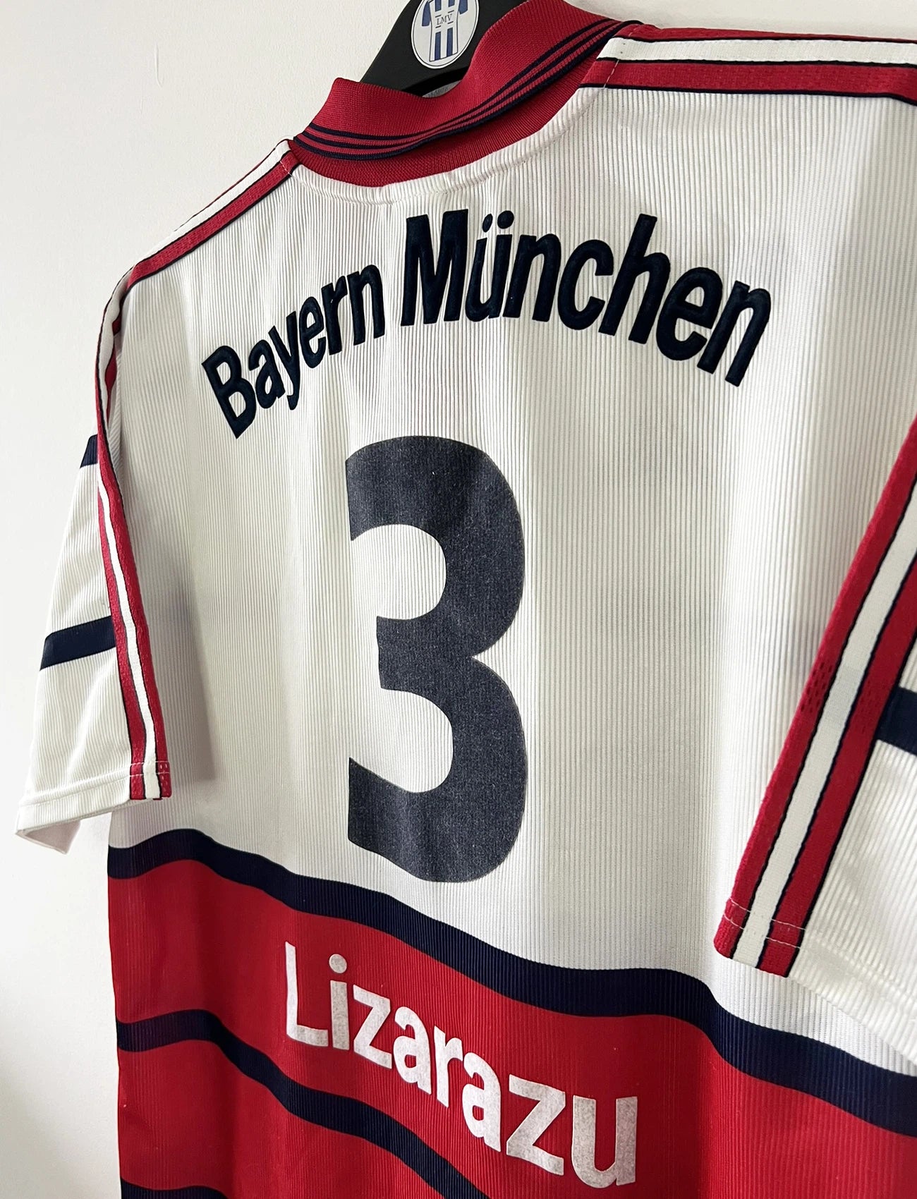 Maillot de foot vintage extérieur blanc et rouge du bayern munich de la saison 1998/1999. On peut retrouver l'équipementier Adidas et le sponsor Opel. Le maillot est floqué du numéro 3 Bixente Lizarazu. Il s'agit d'un maillot authentique d'époque.