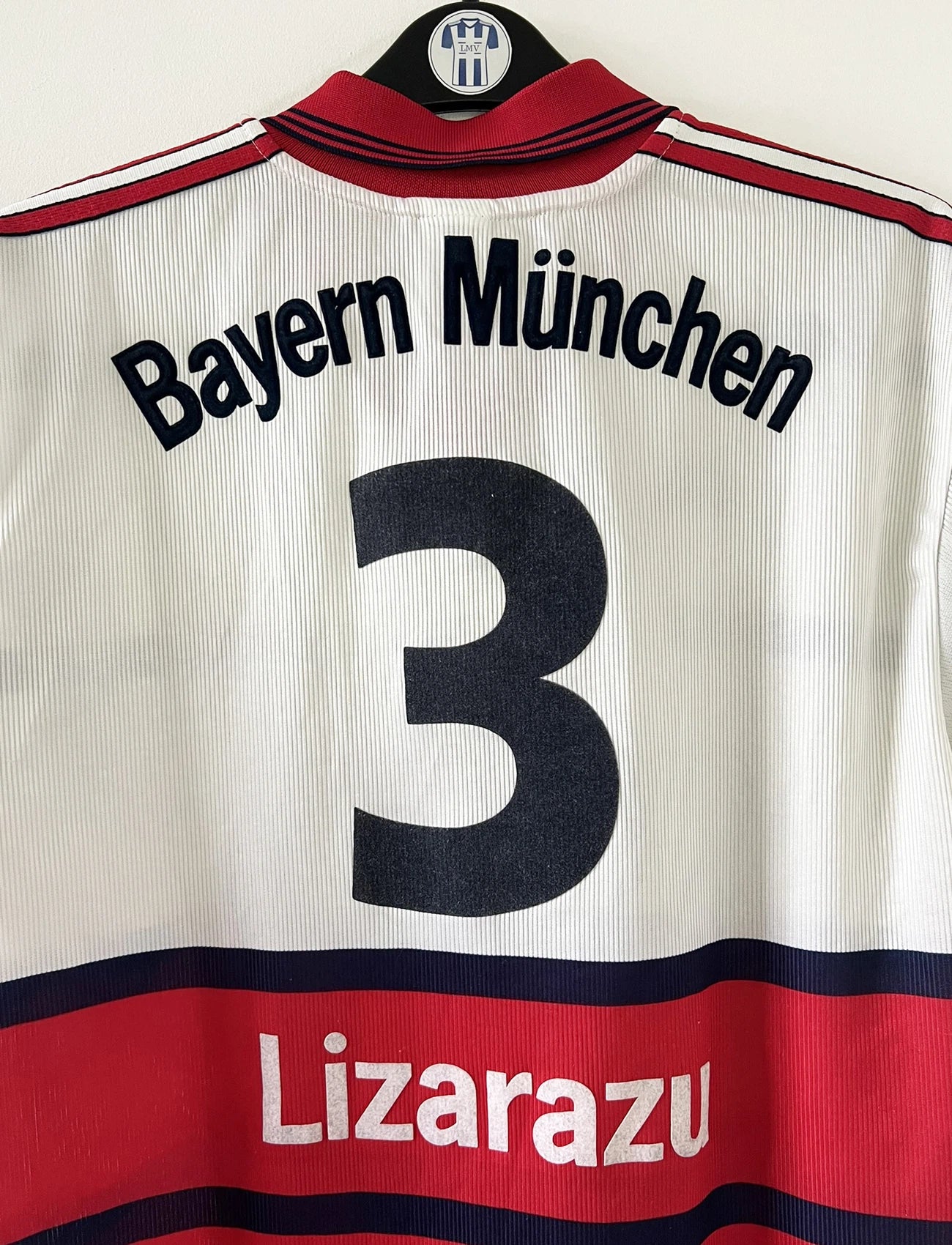 Maillot de foot vintage extérieur blanc et rouge du bayern munich de la saison 1998/1999. On peut retrouver l'équipementier Adidas et le sponsor Opel. Le maillot est floqué du numéro 3 Bixente Lizarazu. Il s'agit d'un maillot authentique d'époque.