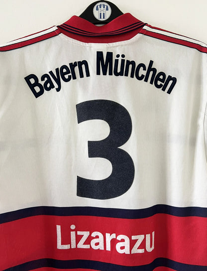 Maillot de foot vintage extérieur blanc et rouge du bayern munich de la saison 1998/1999. On peut retrouver l'équipementier Adidas et le sponsor Opel. Le maillot est floqué du numéro 3 Bixente Lizarazu. Il s'agit d'un maillot authentique d'époque.