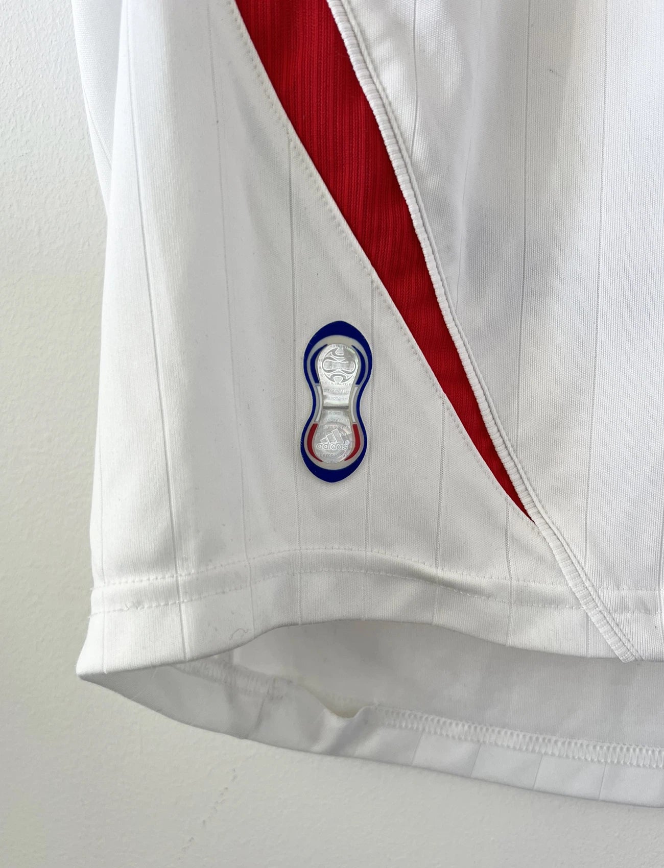Maillot de foot vintage extérieur blanc de l'équipe de France 2006. On peut retrouver l'équipementier Adidas. Il s'agit d'un maillot authentique d'époque comportant l'étiquette 740125