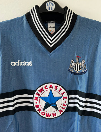 Maillot de foot vintage extérieur bleu de Newcastle de la saison 1996/1997. On peut retrouver l'équipementier Adidas et le sponsor Newcastle Brown Ale. Il s'agit d'un maillot authentique d'époque.
