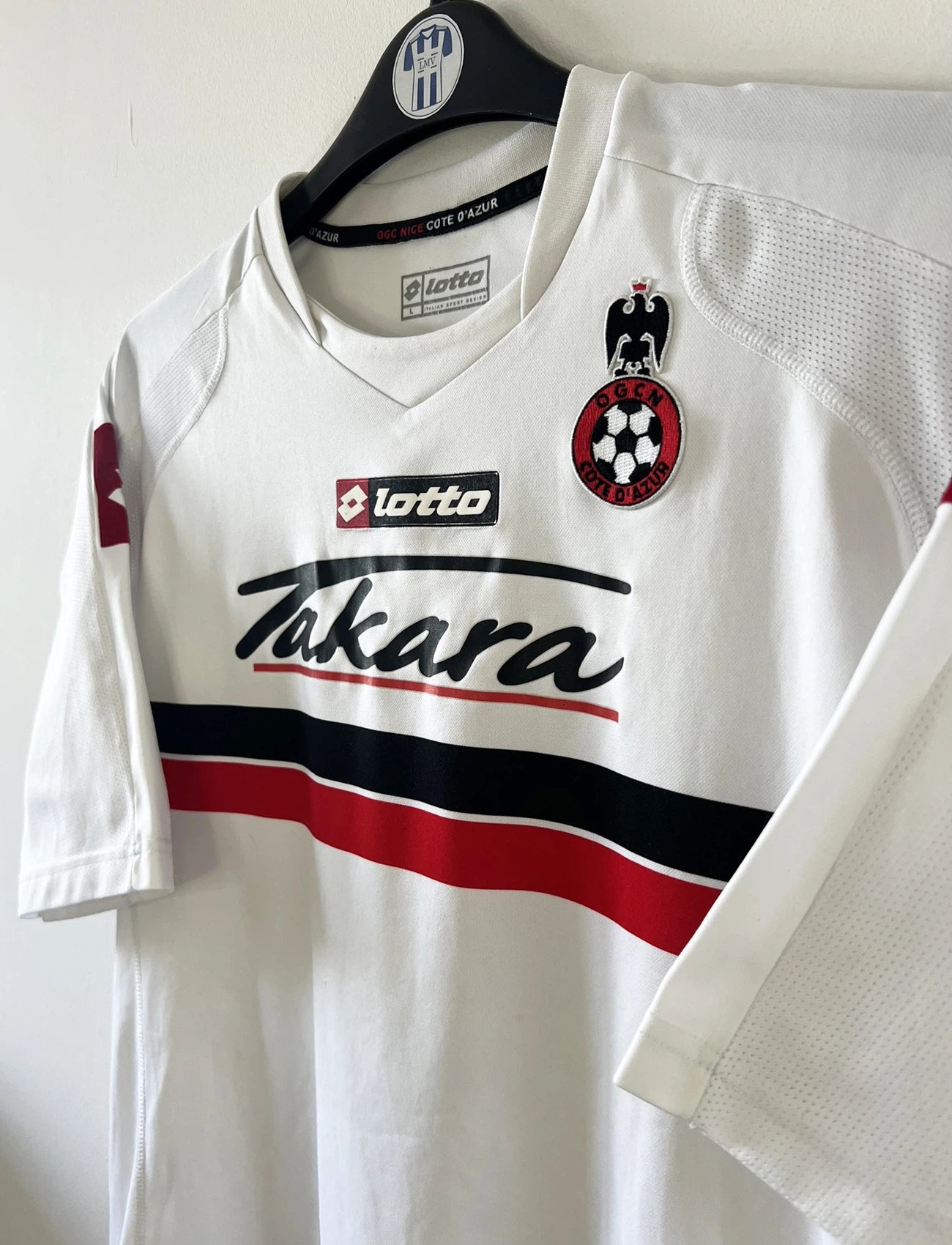 Maillot de foot vintage extérieur blanc de l'ogc nice de la saison 2008/2009. On peut retrouver l'équipementier Lotto et le sponsor Takara. Le maillot est floqué du numéro 6 Echouafni. ll s'agit d'un maillot authentique d'époque.