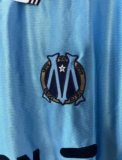 Maillot de foot vintage extérieur bleu de l'Olympique de Marseille de la saison 1998/1999. On peut retrouver l'équipementier Adidas et le sponsor Ericsson. Il s'agit d'un maillot authentique d'époque.